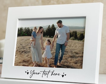 May include: A white rectangular picture frame featuring a horizontal orientation and a smooth finish. The bottom border of the frame displays the black printed text "Your Text here" flanked by two small heart icons on each side of the phrase.