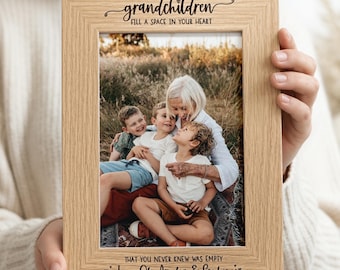 May include: A light-colored wooden picture frame featuring the engraved text "grandchildren FILL A SPACE IN YOUR HEART" at the top and "THAT YOU NEVER KNEW WAS EMPTY Love Oli, Amelia & Sophie" at the bottom, holding a photo of three children.