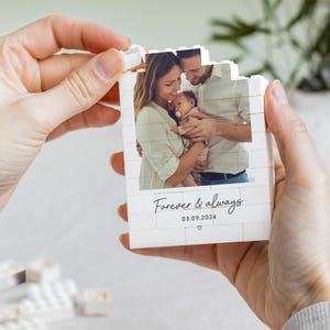 A person's hands holding a small white card with a photograph of a family, and the text "Forever & always" and the date "03.09.2024" printed on it.