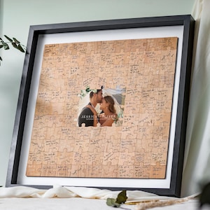 Può includere: Un libro degli ospiti a forma di puzzle in legno quadrato incorniciato in nero, con una foto centrale di una coppia e il testo "JESSICA & OLIVER" e "SATURDAY 24TH AUGUST 2024". I pezzi del puzzle sono pieni di messaggi scritti a mano in inchiostro nero.