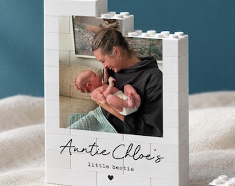 May include: A white building block frame featuring a photograph of a person holding a baby. The frame has the text "Auntie Chloe's" in a script font, "little bestie" in a sans-serif font, and a small black heart icon printed on the front surface.