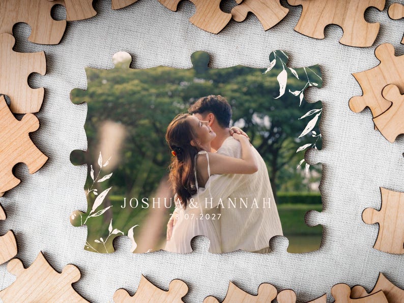 Wedding reception table setup featuring the personalised UV-printed wooden photo puzzle guest book alternative with a photograph of a couple embracing outdoors framed by white botanical leaves alongside pens and the matching wooden instruction stand.