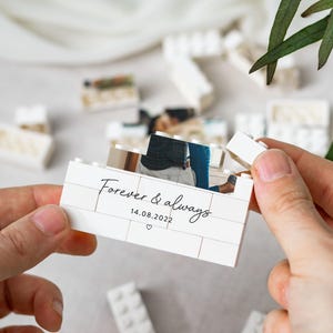 A person's hands holding a small white box with a photo inside, surrounded by scattered white Lego bricks.