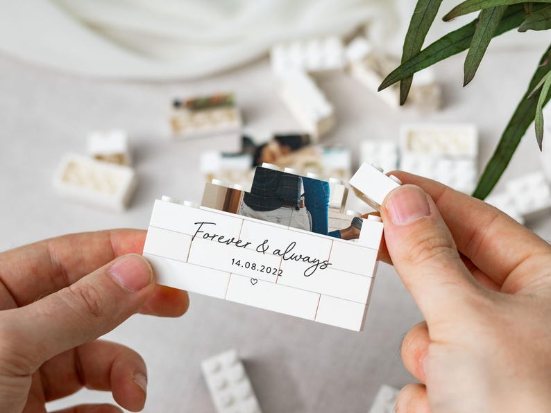 A person's hands holding a small white box with a photo inside, surrounded by scattered white Lego bricks.