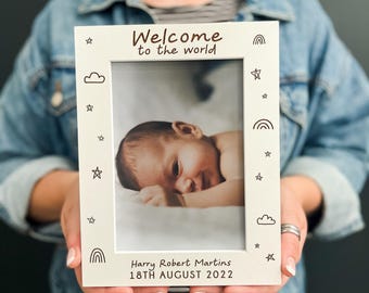 May include: A white rectangular picture frame featuring the text Welcome to the world at the top and Harry Robert Martins 18TH AUGUST 2022 at the bottom. The frame is decorated with small black line drawings of clouds, stars, and rainbows.