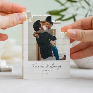 A person is holding a small white photo frame with a photo of a couple embracing, and the frame has the text "Forever & Always" and the date "14.08.2022" printed on it.