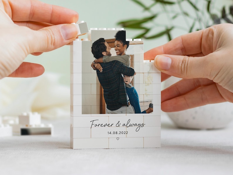 A person is holding a small white photo frame with a photo of a couple embracing, and the frame has the text "Forever & Always" and the date "14.08.2022" printed on it.