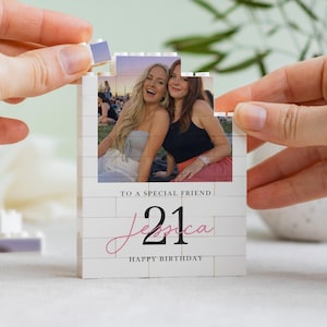 A person's hands are holding a small white card with a photo of two smiling women on it, and the card is being assembled by the person holding it.