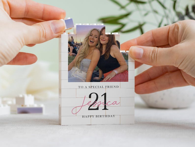 A person's hands are holding a small white card with a photo of two smiling women on it, and the card is being assembled by the person holding it.