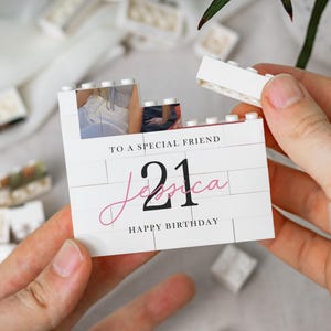 A person's hands holding a white card with a photo and text on it, surrounded by scattered white objects.