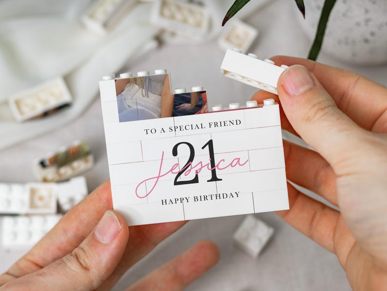 A person's hands holding a white card with a photo and text on it, surrounded by scattered white objects.
