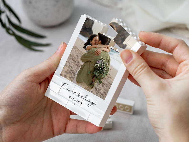 A person's hands holding a white photo frame with a photo of a couple embracing, and the text "Forever & always" and "02.06.2019" printed on it.