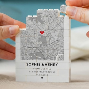 May include: A white building block construction featuring a printed gray map with a red heart icon. The base includes the text SOPHIE & HENRY, PRIMROSE HILL, 51.541257 N, 0.153317 W, 14.09.2018, and a small black heart symbol at the bottom.