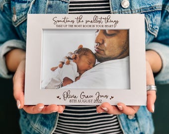 May include: A white rectangular picture frame featuring the black printed text "Sometimes the smallest things TAKE UP THE MOST ROOM IN YOUR HEART" at the top and "Olivia Grace Jones 8TH AUGUST 2022" with small heart icons at the bottom.