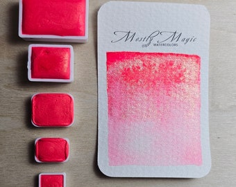 May include: Five watercolour paint pans in different sizes, all filled with a bright pink paint. The paint pans are arranged vertically from largest to smallest. The largest pan is labelled "Mostly Magic Watercolours".
