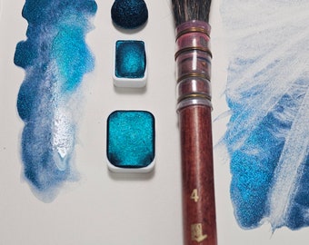 May include: Three watercolor paint pans with a teal blue color, one pan is a round shape and the other two are square. A brush with a wooden handle and black bristles is in the center of the image. The brush handle has the text "Princeton" and the number "4" on it.