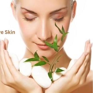 Puede incluir: Una persona con los ojos cerrados sostiene una peque&ntilde;a planta de bamb&uacute; verde y varias piedras ovaladas blancas y lisas en sus manos ahuecadas. El texto "Sensitive Skin" est&aacute; impreso en letras marrones a la izquierda sobre fondo blanco.