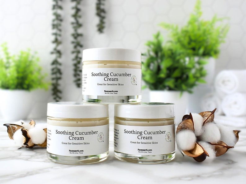 May include: Three white jars of Soothing Cucumber Cream, great for sensitive skin. The jars are on a white marble surface with cotton balls and green plants in the background.