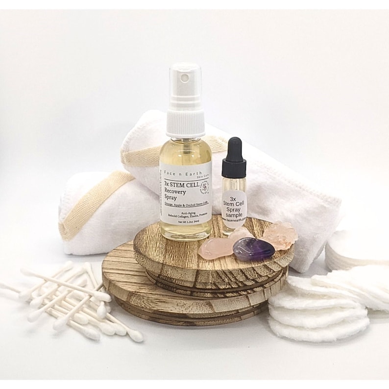 May include: A set of skincare products including a 3x Stem Cell Recovery Spray, a 3x Stem Cell Spray sample, cotton rounds, cotton swabs, and crystals on a wooden platform.
