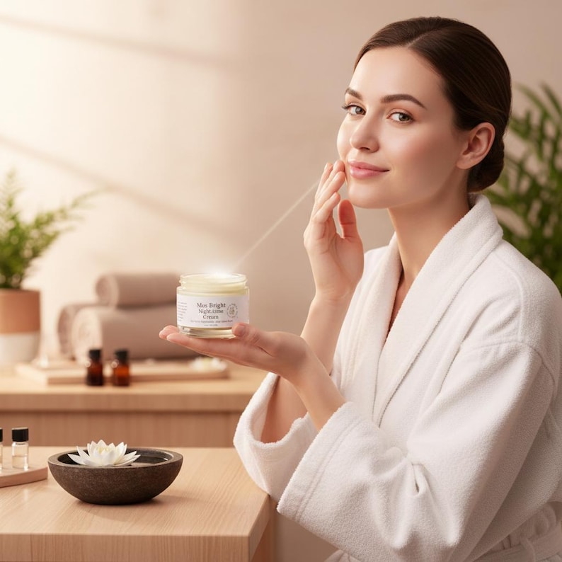 May include: A small, clear glass jar of "Mus Bright Night Glow Cream" with a white label and a light-colored cream inside. The jar is held in a palm, showcasing its compact size and simple design, featuring clear text on the label against a neutral background.