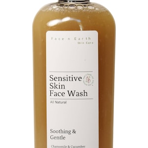 May include: A clear plastic bottle filled with a brownish, translucent liquid face wash. The white label reads Face n Earth Skin Care, Sensitive Skin Face Wash, All Natural, Soothing & Gentle, Chamomile & Cucumber Extracts, Net Wt 6.5oz.