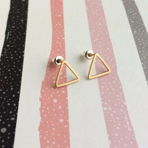 Puede incluir: Un par de pendientes de tri&aacute;ngulo dorado con un dise&ntilde;o simple y minimalista. Los pendientes est&aacute;n sobre un fondo a rayas.