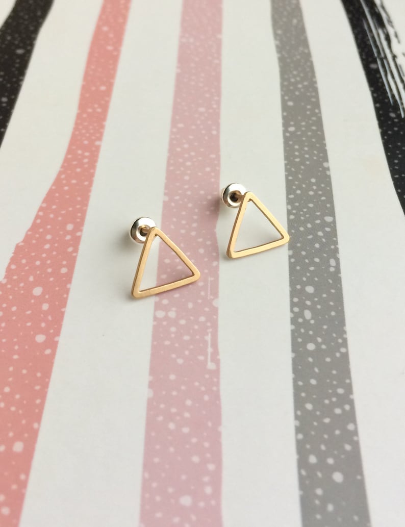 Puede incluir: Un par de pendientes de tri&aacute;ngulo dorado con un dise&ntilde;o simple y minimalista. Los pendientes est&aacute;n hechos de un alambre delgado y tienen una forma geom&eacute;trica delicada.
