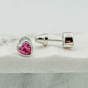 May include: A pair of silver heart-shaped stud earrings with pink cubic zirconia stones.