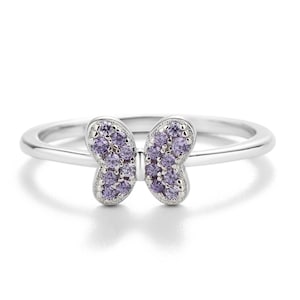 May include: A silver-toned ring featuring a butterfly-shaped centerpiece. The butterfly wings are encrusted with small, round, light purple stones set within a polished metal frame, connected to a smooth, thin, circular band.