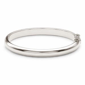 May include: A polished silver-tone bangle bracelet with a smooth, rounded surface and a hinged clasp mechanism on the side. The bracelet features a continuous circular design with a reflective metallic finish and a secure, integrated locking closure.