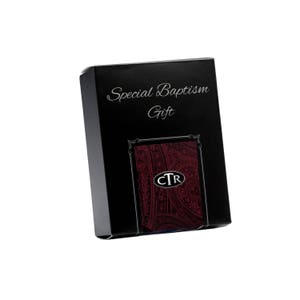 Könnte beinhalten: Eine schwarze Geschenkbox mit dem Schriftzug "Special Baptism Gift" in eleganter Schrift. Die Box zeigt ein bordeauxfarbenes Paisley-Muster mit den Initialen "CTR". Die Geschenkbox ist leicht angewinkelt.