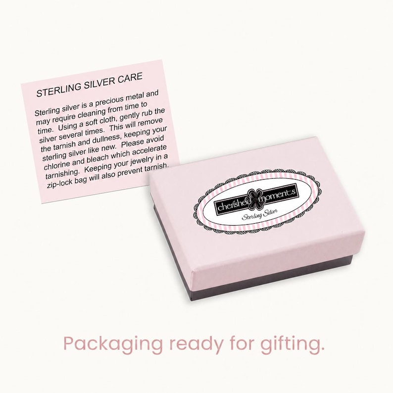 May include: A light pink rectangular jewelry box with a black and white oval logo reading cherished moments Sterling Silver. Beside the box is a square card with the heading STERLING SILVER CARE and instructions for cleaning and maintenance.