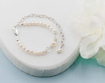 May include: A delicate bracelet featuring a strand of small, white, oval-shaped freshwater pearls interspersed with clear, faceted crystal beads. The bracelet includes a silver-toned metal chain extender with a lobster clasp and a single pearl charm.