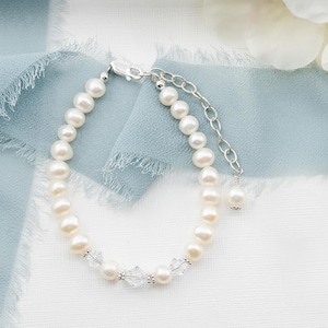 May include: A bracelet featuring a strand of white freshwater pearls interspersed with clear faceted crystal beads. The piece includes a silver-toned metal lobster claw clasp and an adjustable chain extension finished with a single pearl drop.