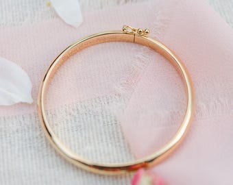 Puede incluir: Una pulsera dorada con cierre de broche. La pulsera está grabada con las palabras "My Forever Valentine 09/06/2018". La pulsera está sobre una tela rosa con pétalos de flores.