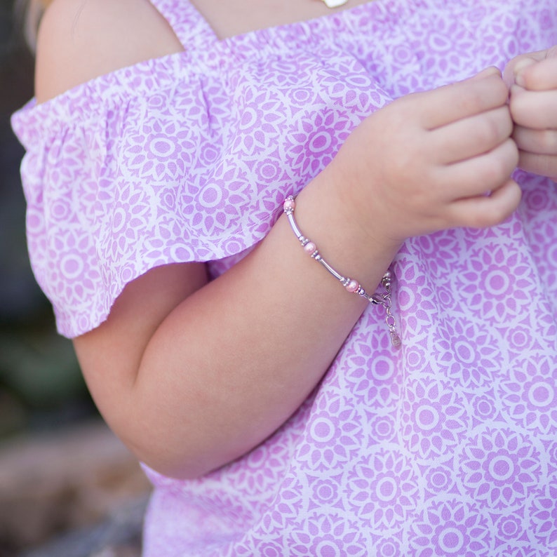Little girl wearing sterling silver bracelet with long silver beads and pink pearl accents.