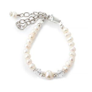 Op de afbeelding: Een armband met witte zoetwaterparels, heldere gefacetteerde kristalkralen en kleine zilverkleurige metalen tussenstukjes. Het sieraad is voorzien van een zilverkleurige karabijnsluiting en een verstelbare ketting met een enkele parel.