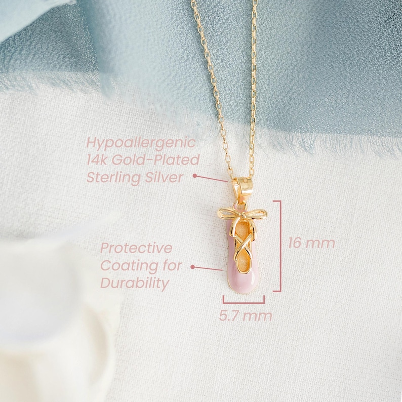 May include: A gold-plated sterling silver necklace featuring a ballet slipper pendant with a pink enamel finish and a gold bow detail. The pendant measures 16 mm in height and 5.7 mm in width. Text indicates hypoallergenic material and a protective coating.