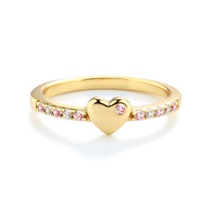 May include: A gold ring featuring a heart-shaped design with a single pink stone at its centre. The band is decorated with a row of small pink and white stones.