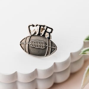 May include: Silver football pin with the word "CTR" on top. The football has laces and a textured surface.