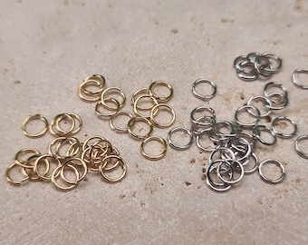 May include: A collection of gold and silver jump rings. The jump rings are small and round, and they are perfect for jewelry making.