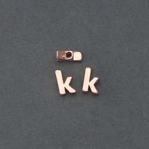 May include: Two gold-coloured letter charms in the shape of the letter "K". A small gold-coloured connector charm is also included.