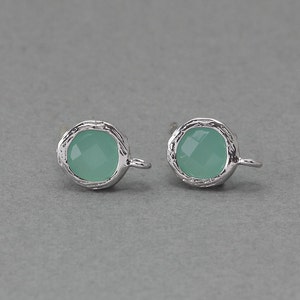 Könnte beinhalten: Ein Paar silberne Ohrringe mit jeweils einem hellgrünen Edelstein. Die Ohrringe haben eine strukturierte, organische Form.