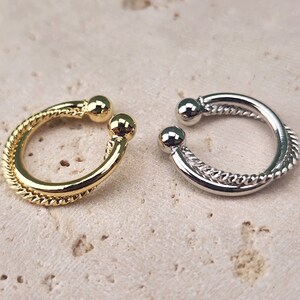 May include: Two ear cuffs, one gold and one silver, with a twisted rope design. The cuffs are open and have a ball at each end.