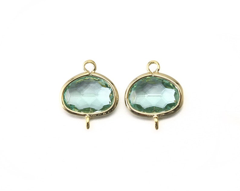 K&ouml;nnte beinhalten: Zwei ovale, hellblaue Glasanh&auml;nger mit goldfarbenen Metalleinstellungen und Sprungringen. Die Anh&auml;nger haben ein facettierten Design.