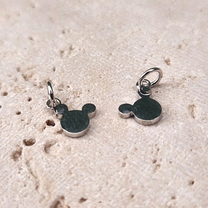May include: Two silver charms in the shape of Mickey Mouse's head. The charms have a loop at the top for attaching to a bracelet or necklace.