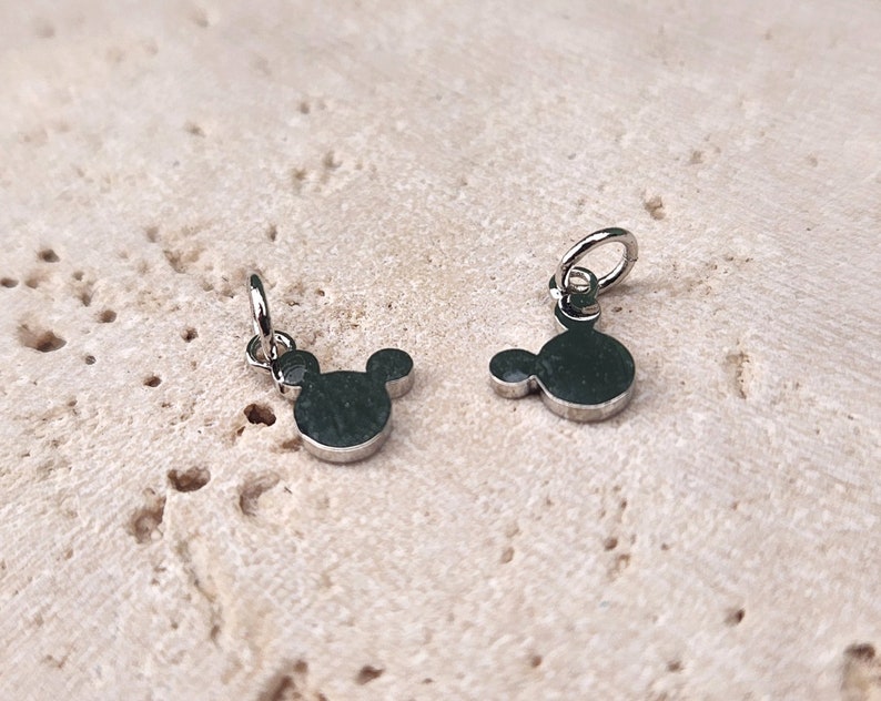 May include: Two silver charms in the shape of Mickey Mouse's head. The charms have a loop at the top for attaching to a bracelet or necklace.