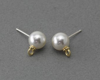 Op de afbeelding: Een paar parel oorknopjes. Elke oorbel heeft een witte, bolvormige parel met een goudkleurige lus en een zilveren pin. De oorbellen staan tegen een grijze achtergrond.