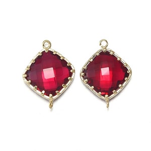 May include: Two gold-toned pendant charms with a red faceted glass square in the centre. The charms have a loop at the top for attaching to a necklace or bracelet.