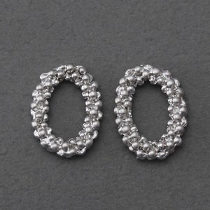 May include: A pair of silver hoop earrings made of small, round beads. The earrings are oval shaped and have a smooth, polished finish.